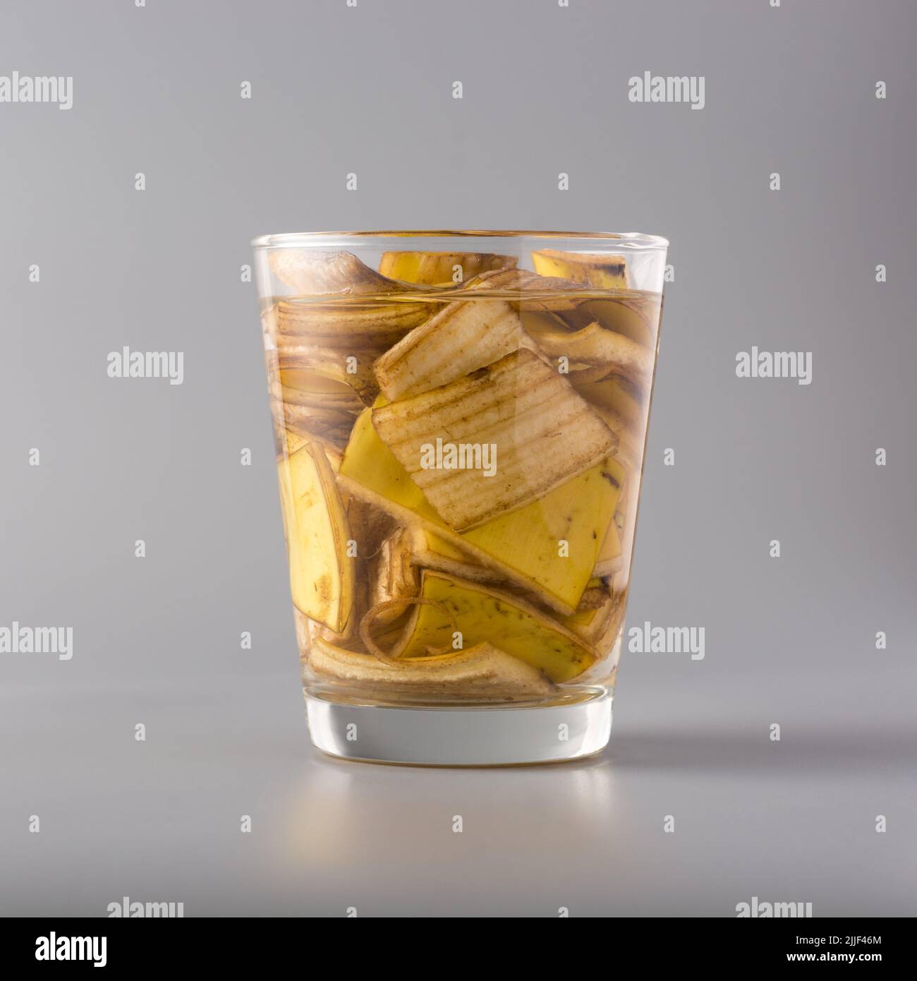 cut banana peels pieces soaked in glass of water isolated on gray