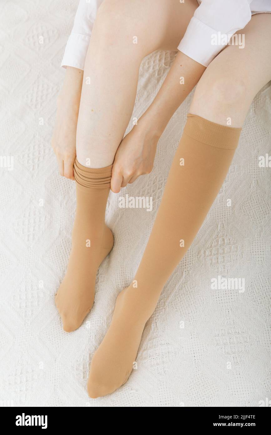 Knee socks or socks. Beige compression stockings on a woman in a white room. Girl putting on stockings at home. Beautiful female legs Stock Photo