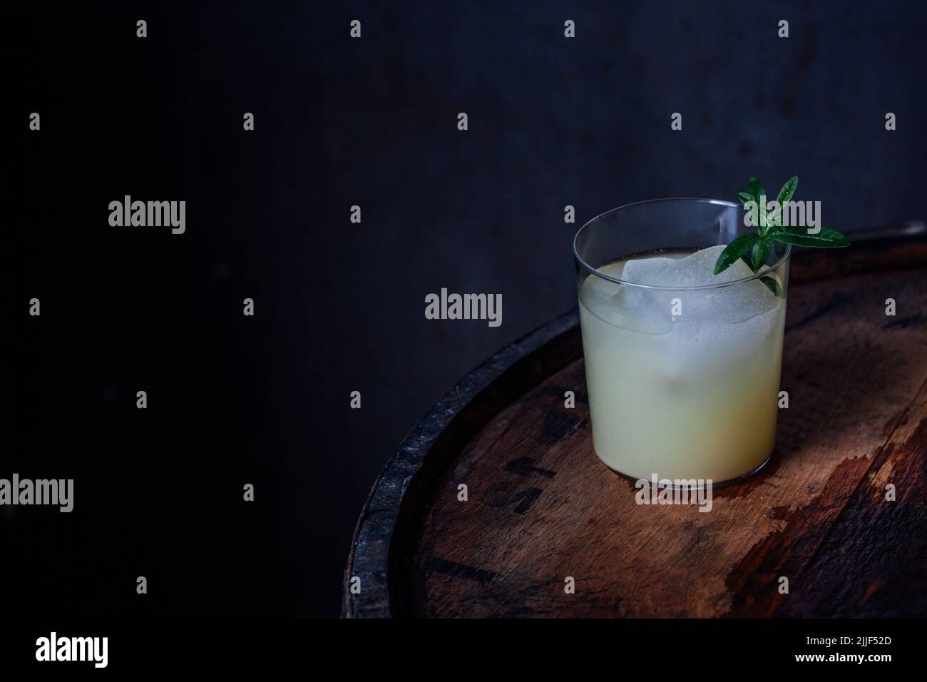 glass of ginger beer Moscow mule with large ice and lemon verbena herb garnish on wood barrel dark background Stock Photo