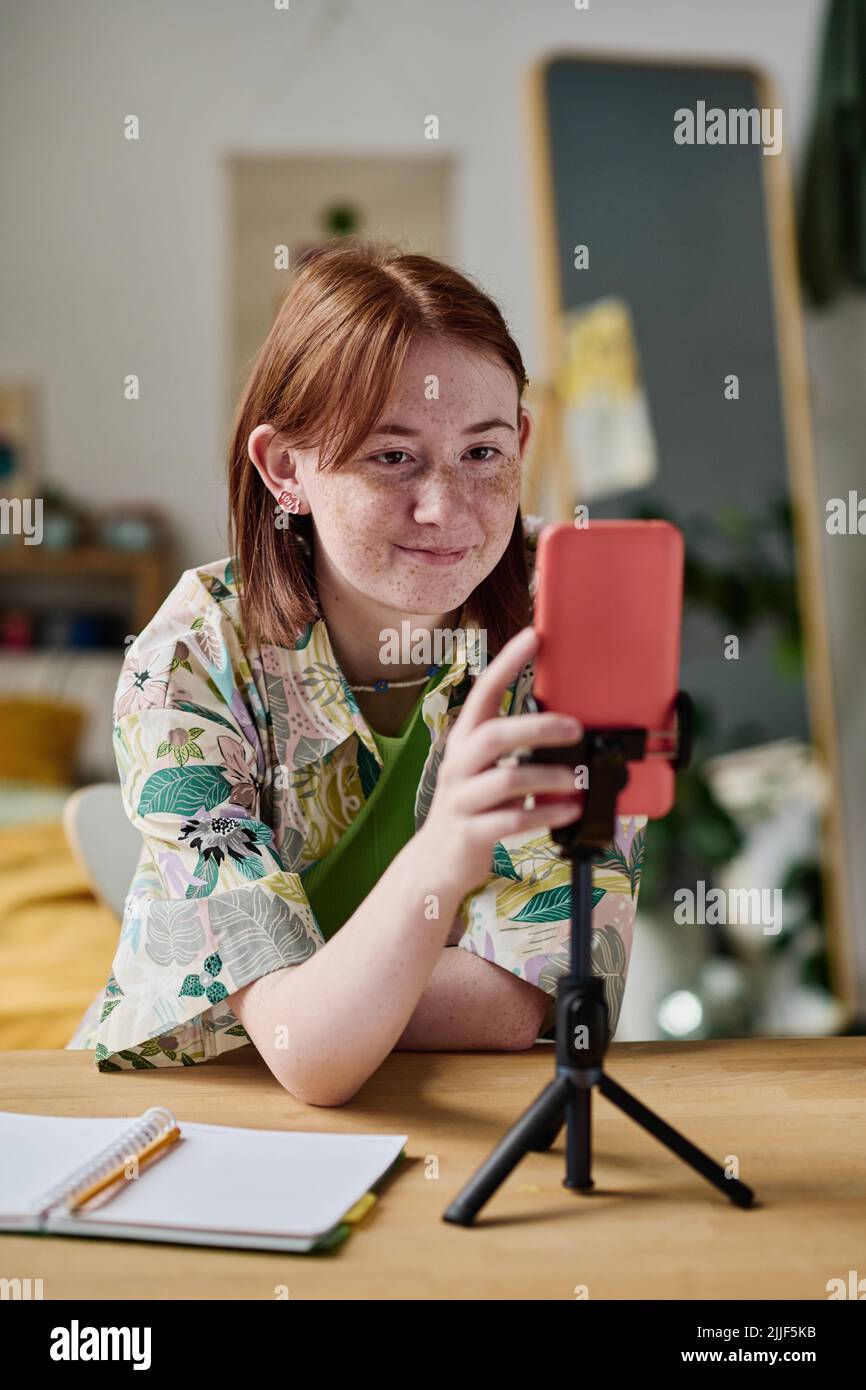 Teenage girl using her smartphone on tripod to recording blog at table