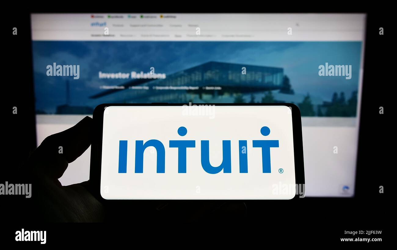 Person holding smartphone with logo of US financial software company Intuit Inc. on screen in front of website. Focus on phone display. Stock Photo