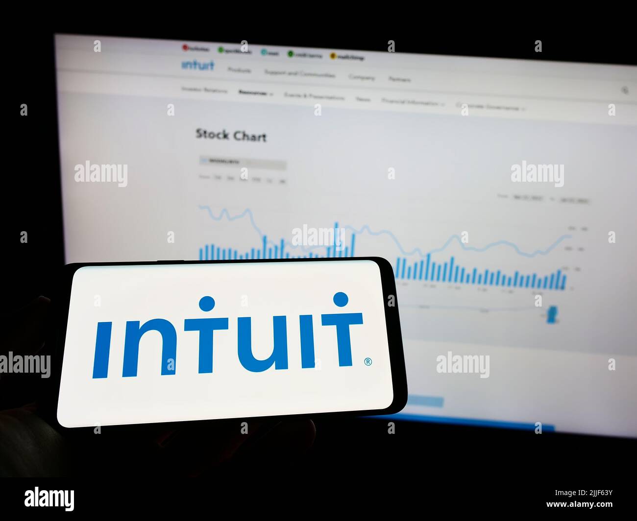 Person holding mobile phone with logo of American financial software company Intuit Inc. on screen in front of web page. Focus on phone display. Stock Photo