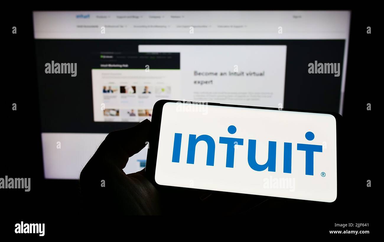 Person holding cellphone with logo of US financial software company Intuit Inc. on screen in front of business webpage. Focus on phone display. Stock Photo