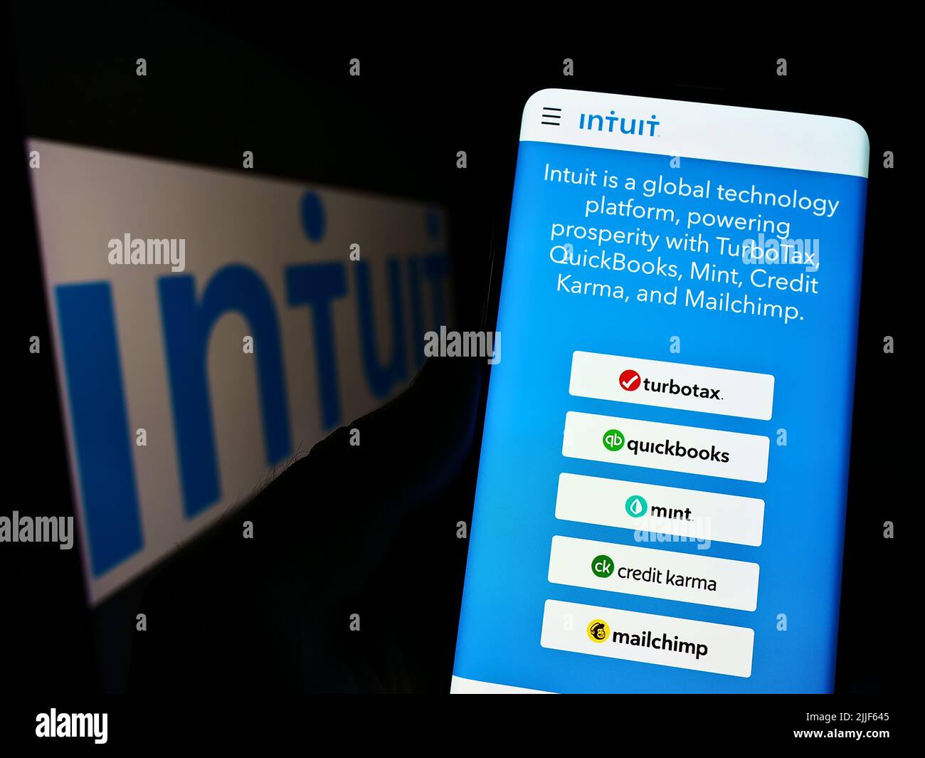 Person holding cellphone with webpage of US financial software company Intuit Inc. on screen in front of logo. Focus on center of phone display. Stock Photo