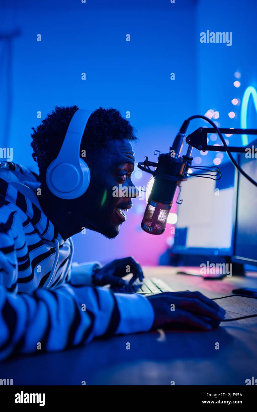 African excited gamer boy in headset speaking in microphone to audience