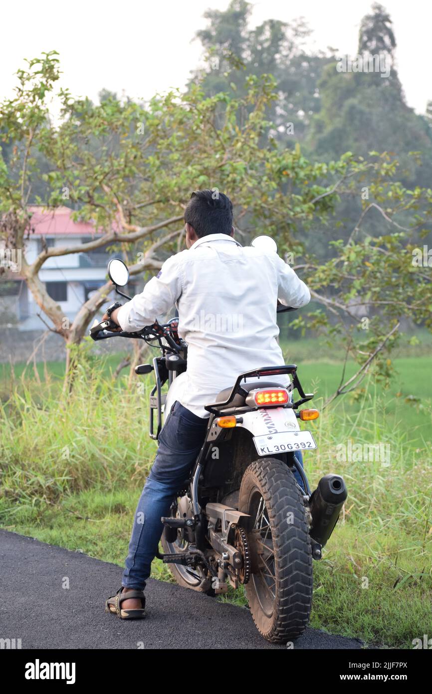 Rear view of an indian young man riding a motorcycle near a paddy field ...