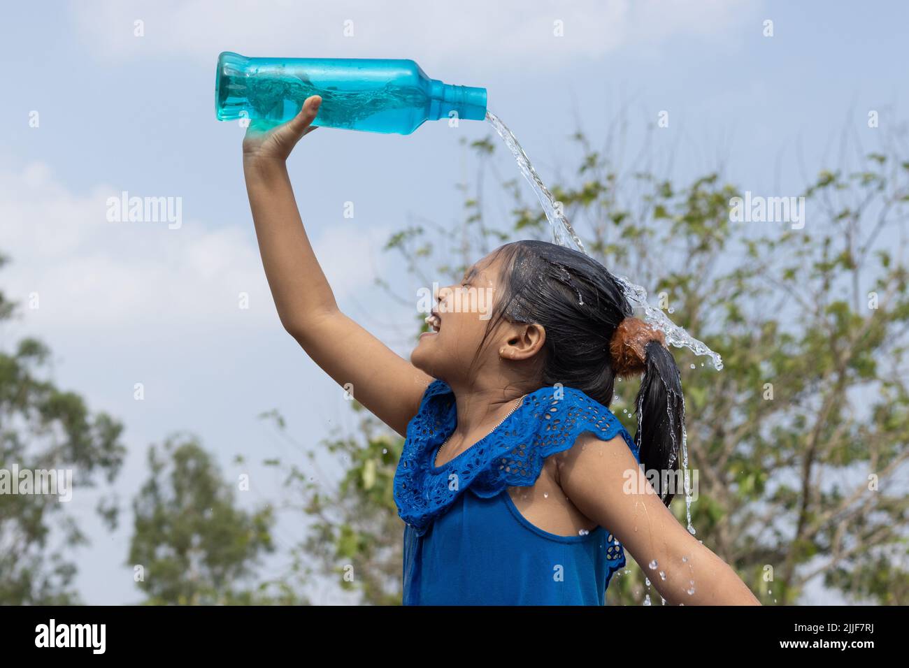 An Indian girl pouring water on head from a blue plastic bottle under