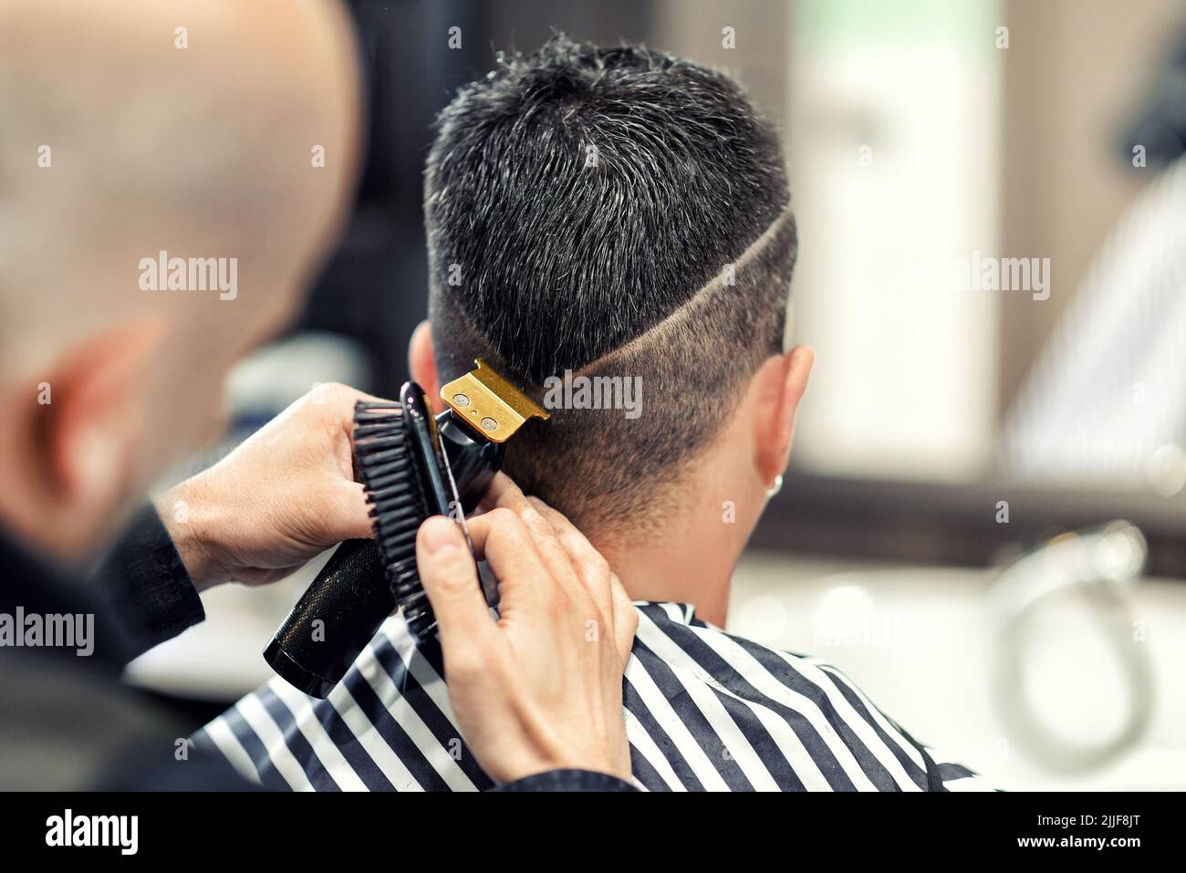 Unrecognizable male barber using trimmer and brush to shave ornament on head of man during work in barbershop Stock Photo