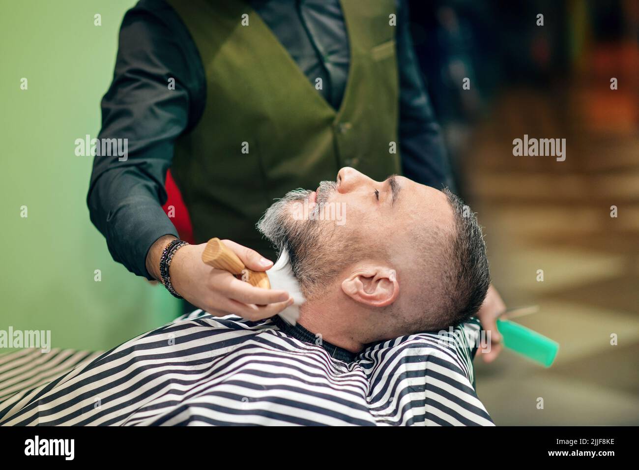 Crop barber removing beard hair from neck of man during work in barbershop Stock Photo