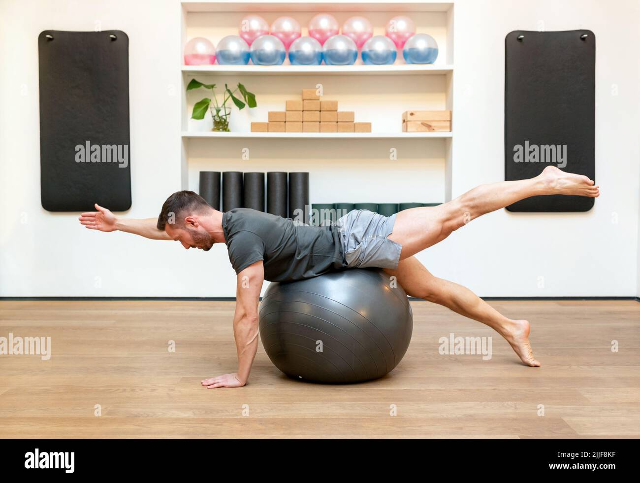 Fit man doing diagonal stabilization exercises on a Pilates ball in a gym in a healthy active lifestyle concept Stock Photo