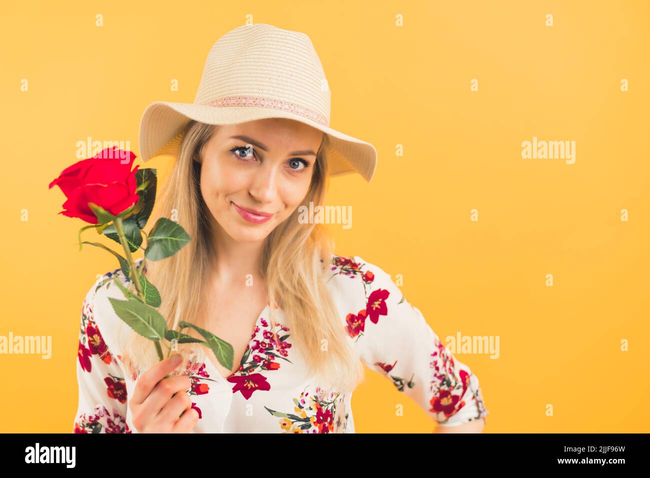 A blondie girl wearing a hat and holding a beautiful rose on an orange background looking at the camera . High quality photo Stock Photo