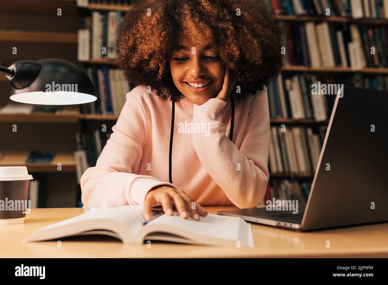 Smiling girl sitting at desk and reading in library Stock Photo - Alamy