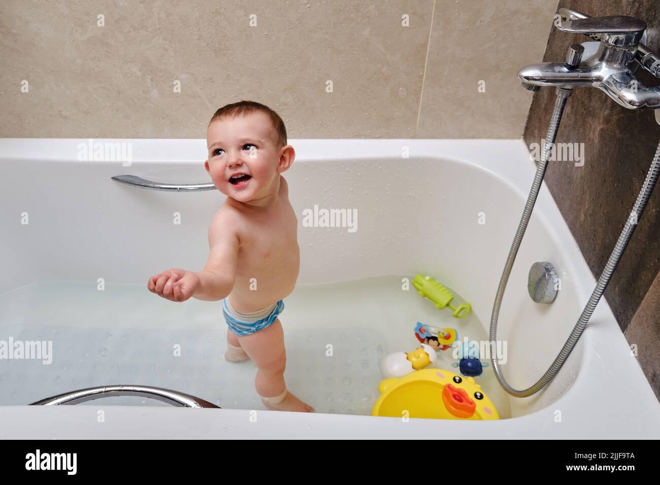 Happy toddler baby boy is playing with toys in the bathtub. A smiling
