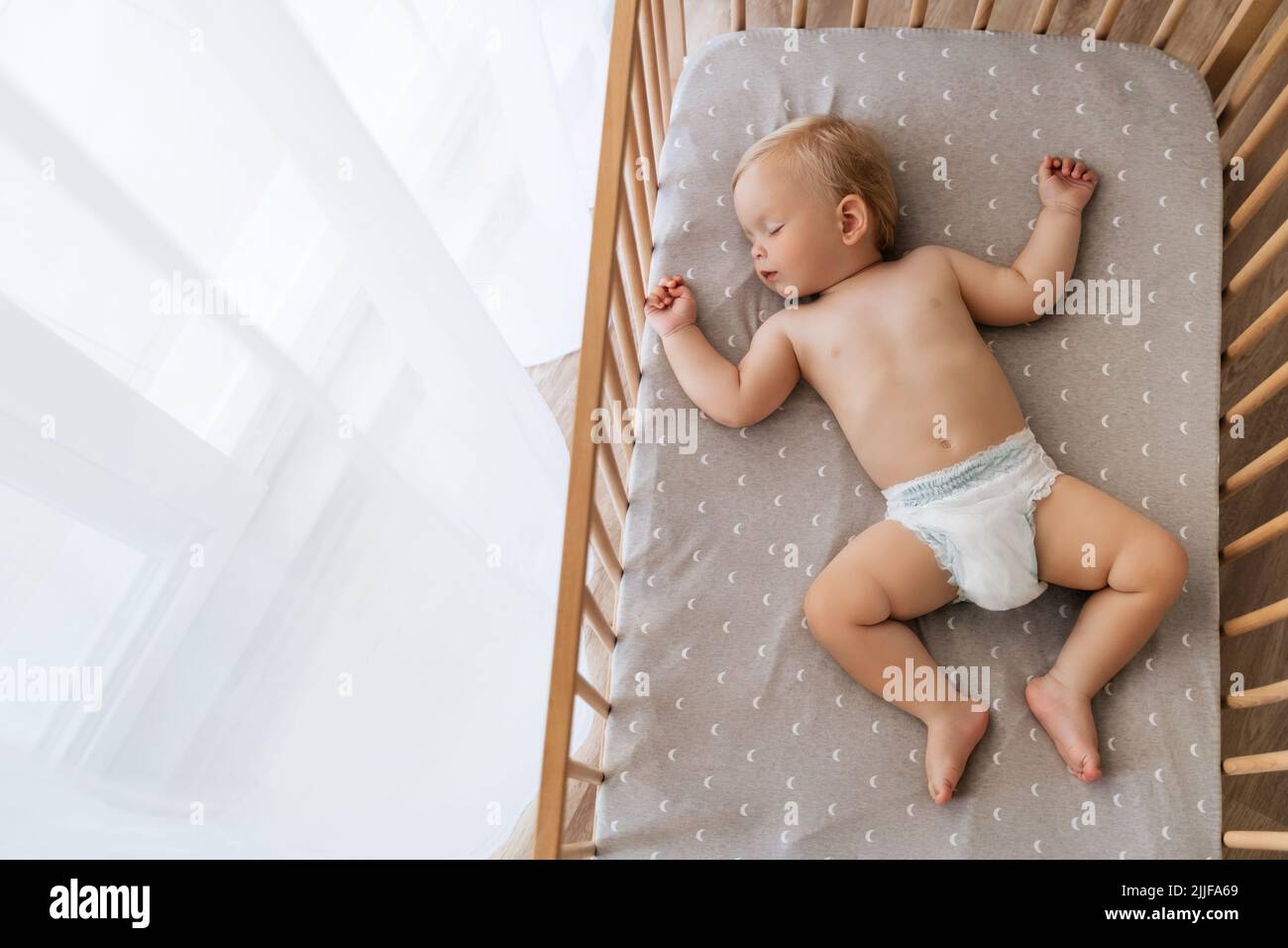 Upper view copy space portrait of cute blond baby sleeping in bed on his back, feeling safe, watching sweet dreams, resting, growing, gaining strength, getting strong. Childcare concept. Nap time Stock Photo