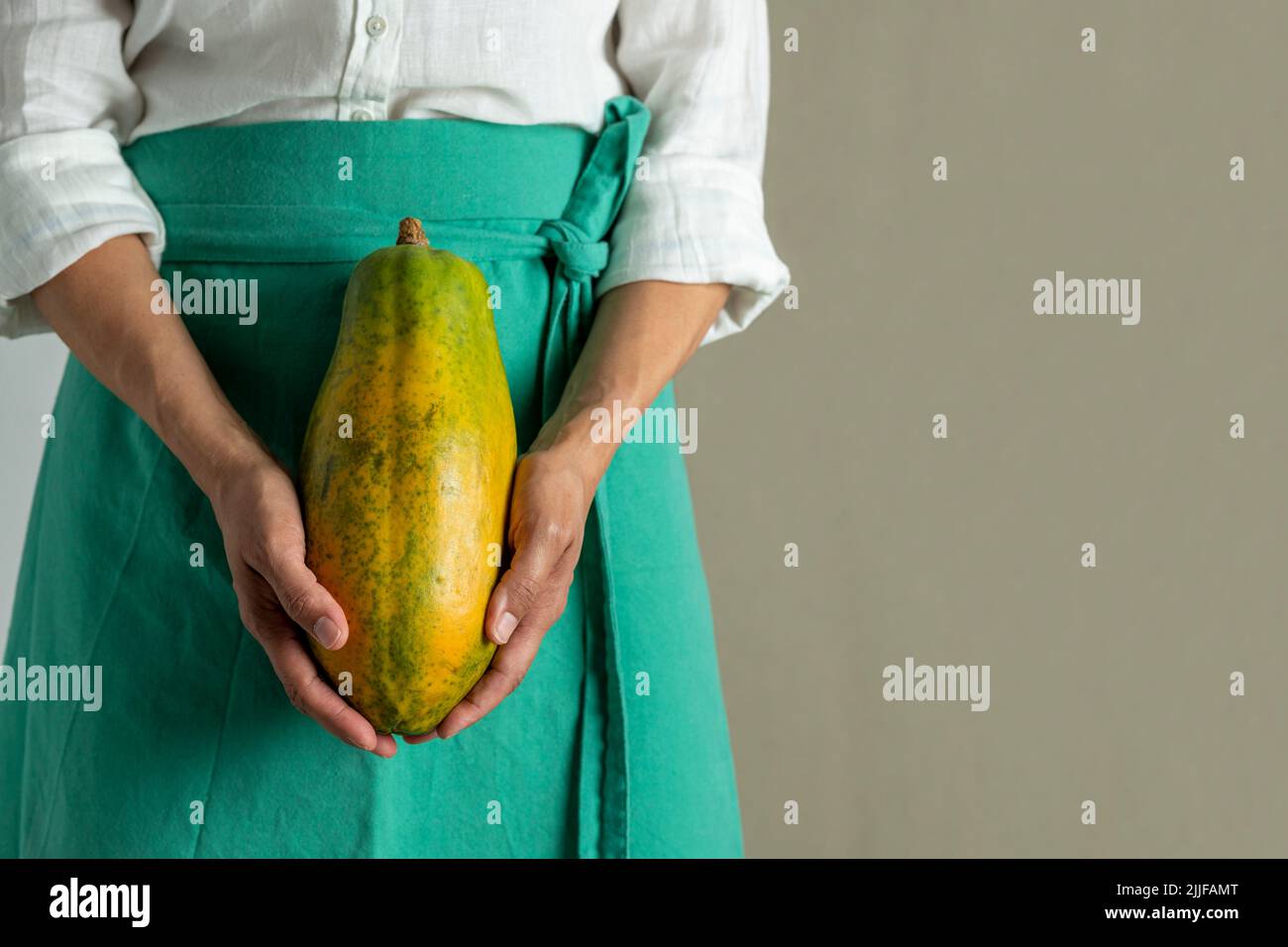 Close-up of a woman holding a papaya against plain background - stock photo Stock Photo