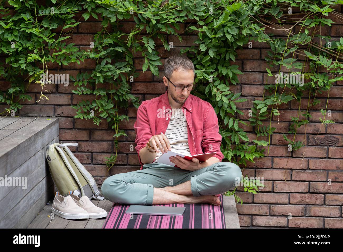 Young relaxed student guy sitting in lotus pose reading book outdoors, enjoying studying outside Stock Photo