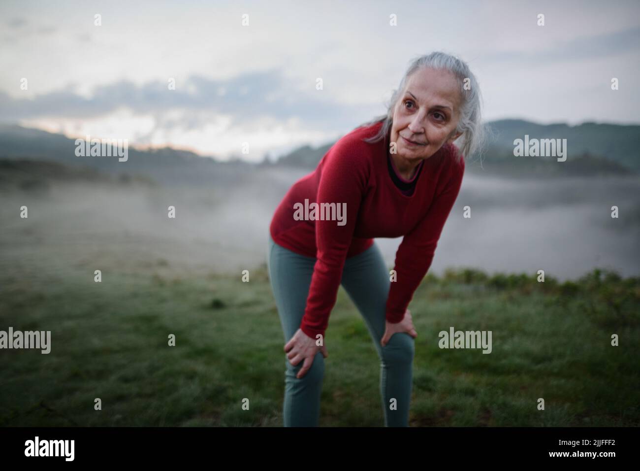 Senior woman doing breathing exercise in nature on early morning with