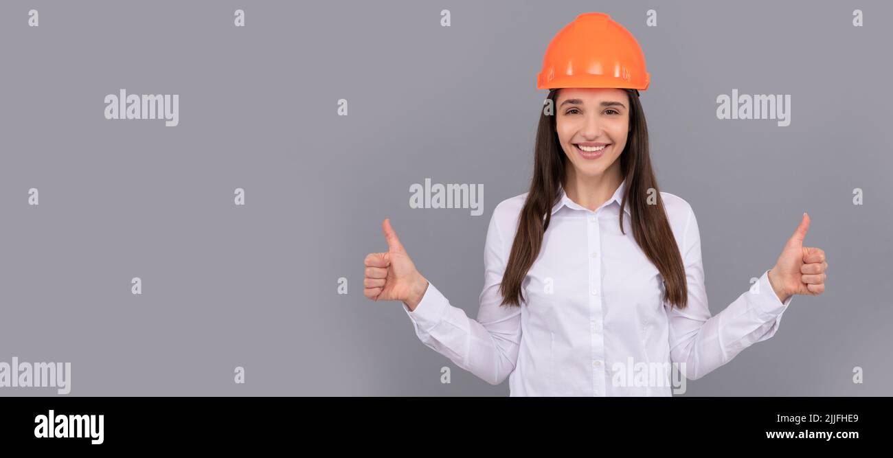 happy woman in protective helmet and white shirt showing thumb up gesture, good result. Woman isolated face portrait, banner with mock up copy space. Stock Photo