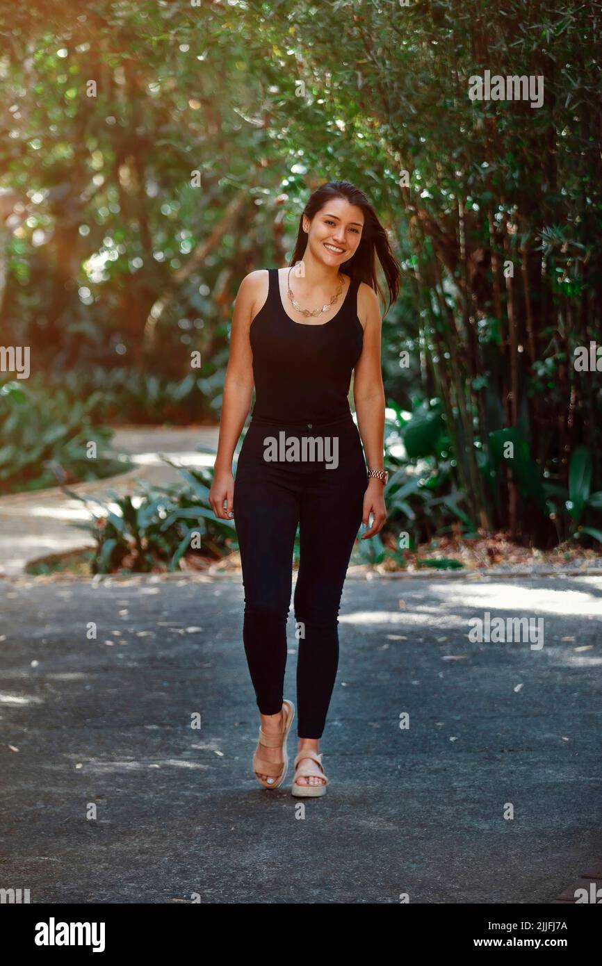 young Latina woman dressed in black jeans and tank top walking in a park in Costa Rica Stock Photo