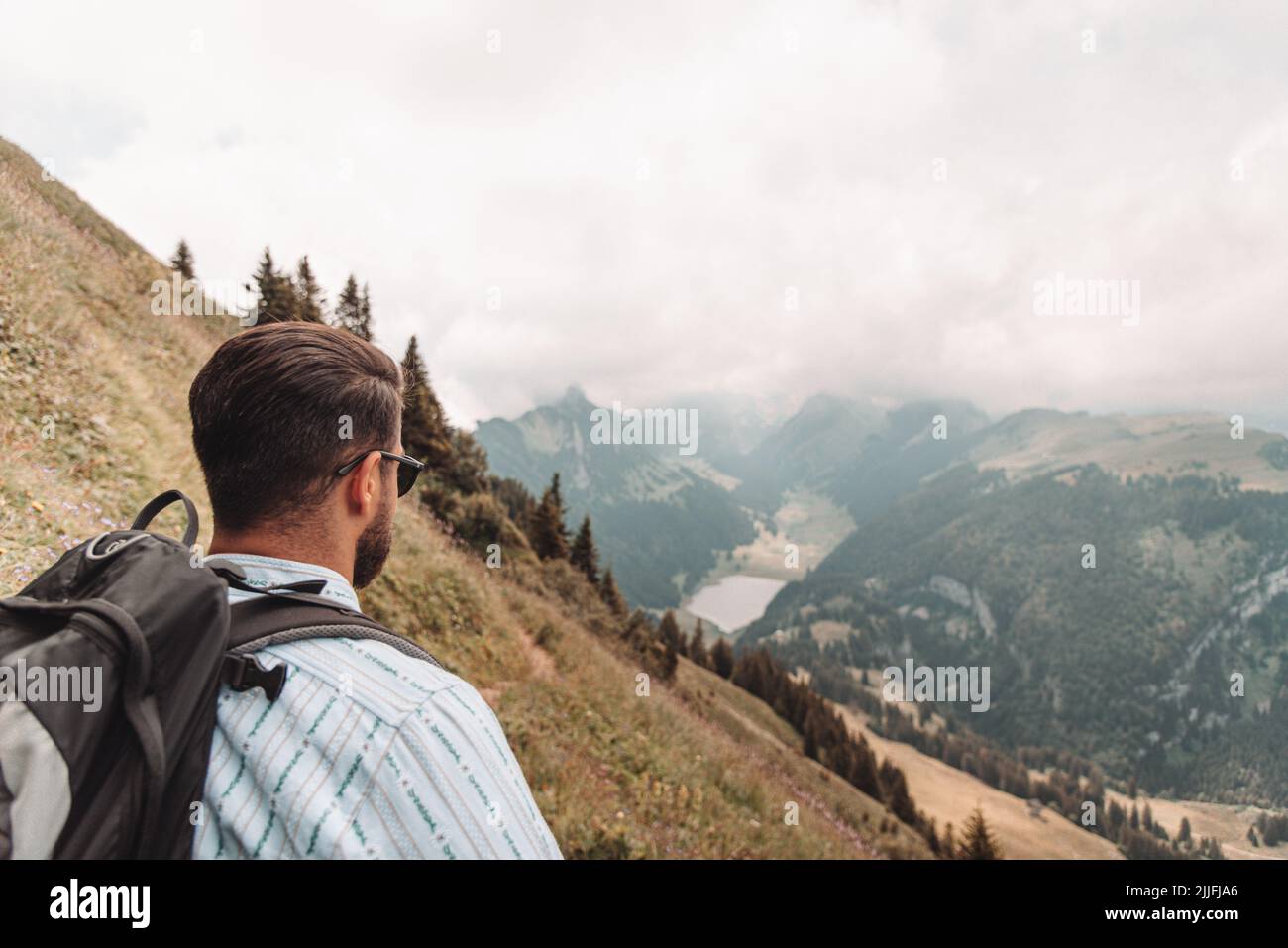 A young man hiking in the Appenzell Alps in Switzerland in cloudy sky background Stock Photo