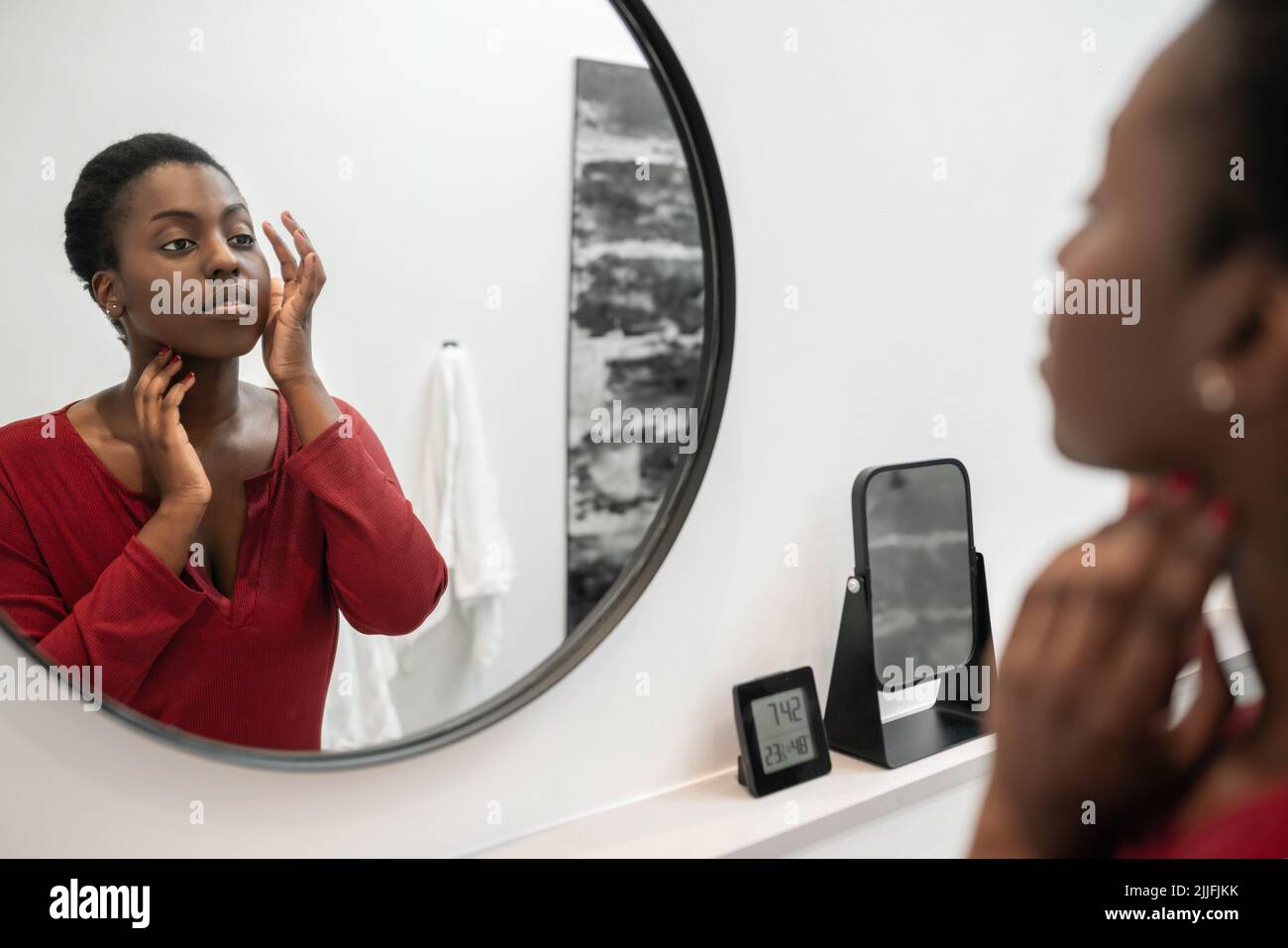Reflection in mirror of Black African woman touching and inspecting her face. Self care and skin care. Morning routine Stock Photo
