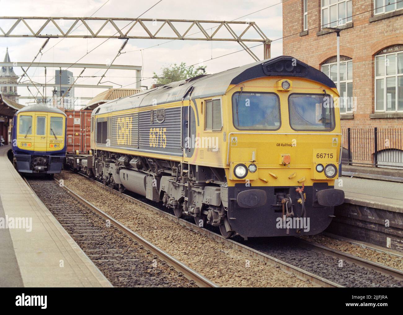 Manchester, UK - June 2022: A diesel locomotive (Class 66 66715) pulled a container train past Deansgate station, a passenger train in the rear. Stock Photo