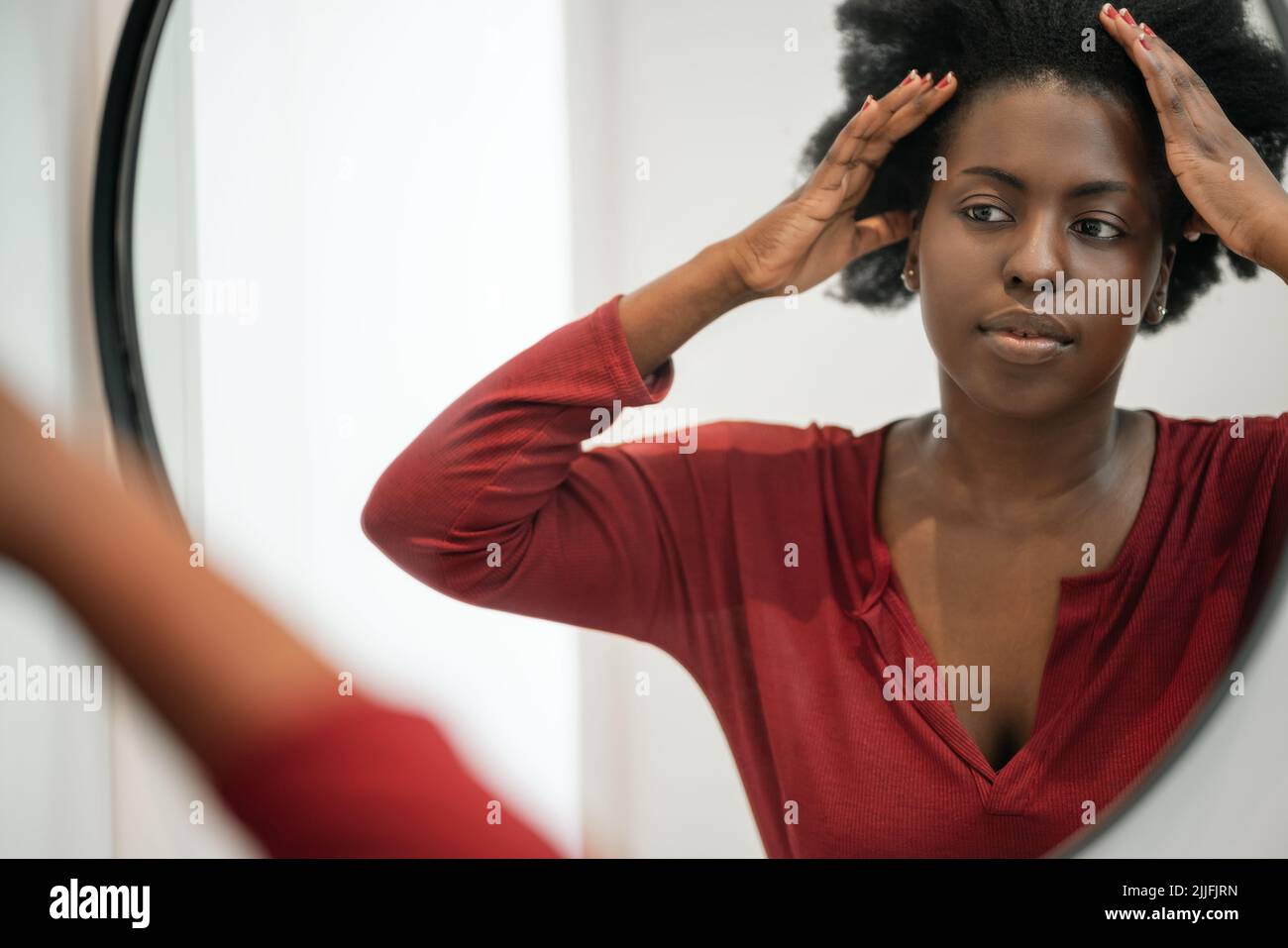 Mourning routine of Black African woman fixing her hair and looking into bathroom mirror. Hair styling and getting ready Stock Photo