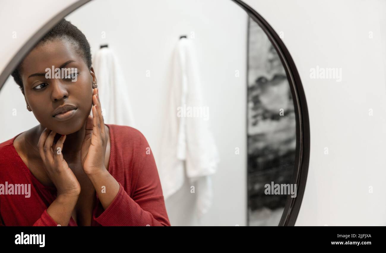 Reflection in mirror of Black African woman touching and inspecting her face. Self care and skin care Stock Photo