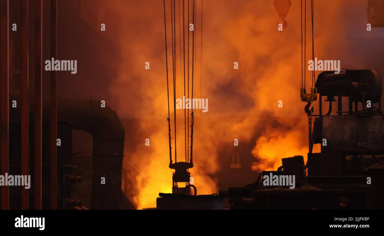 Metallurgical heavy industry background. Large dark workshop of foundry factory in puffs of orange smoke from blast furnace. Stock Photo