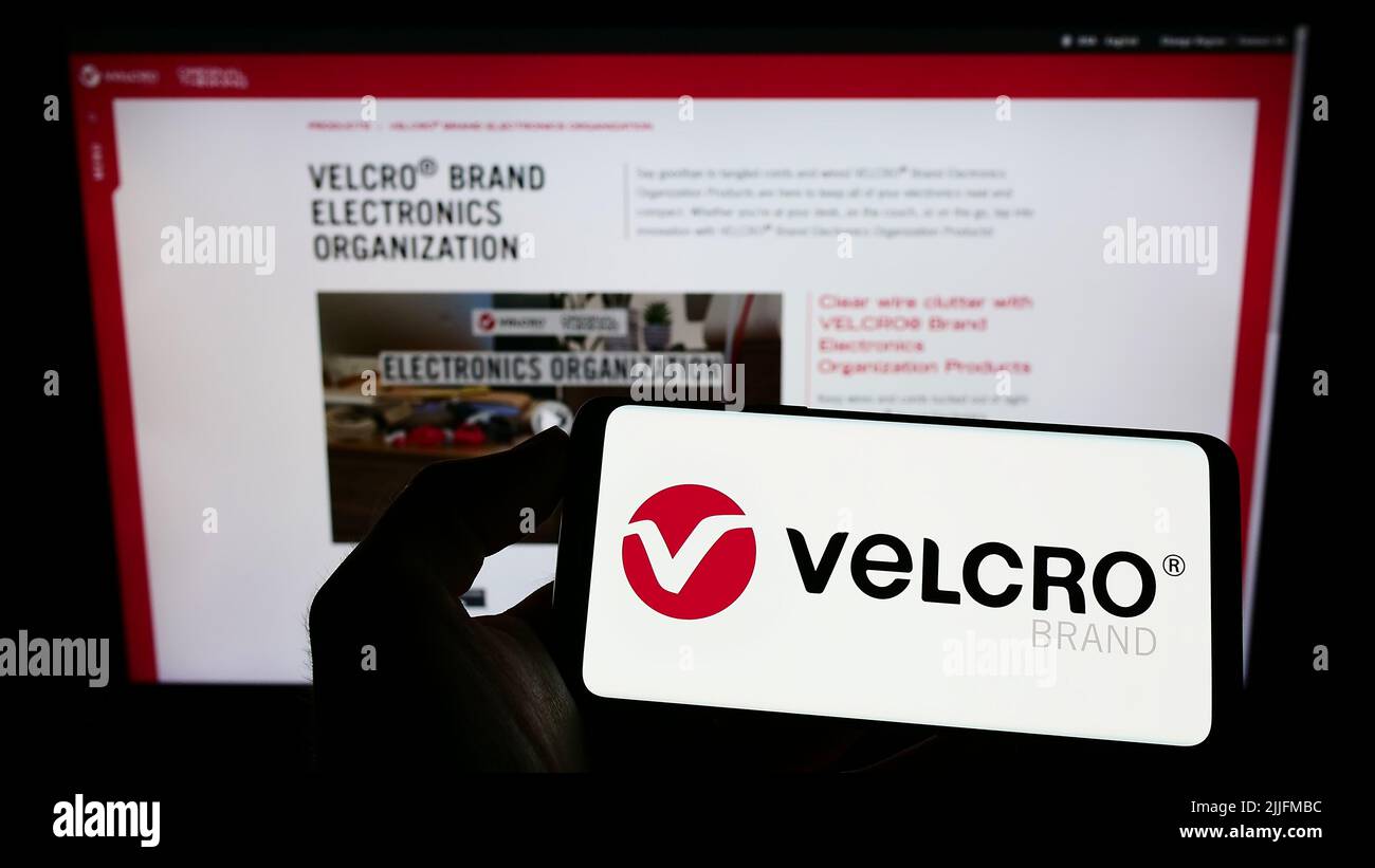 Person holding cellphone with logo of British company Velcro IP Holdings LLC on screen in front of business webpage. Focus on phone display. Stock Photo
