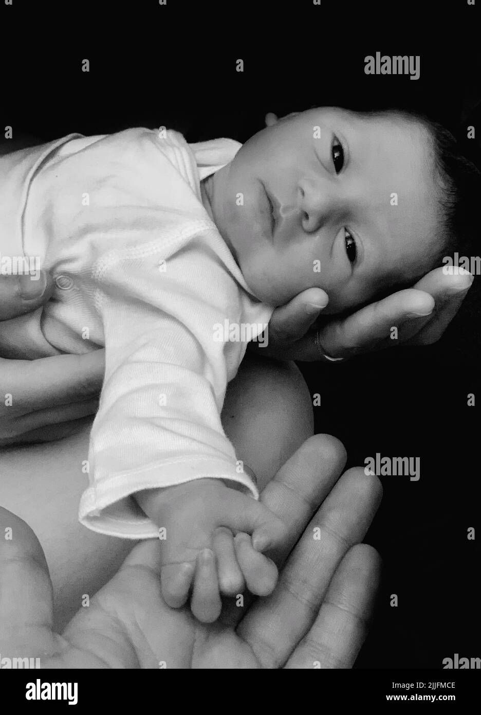 A vertical black and white shot of hands holding a newborn baby in a dark background Stock Photo