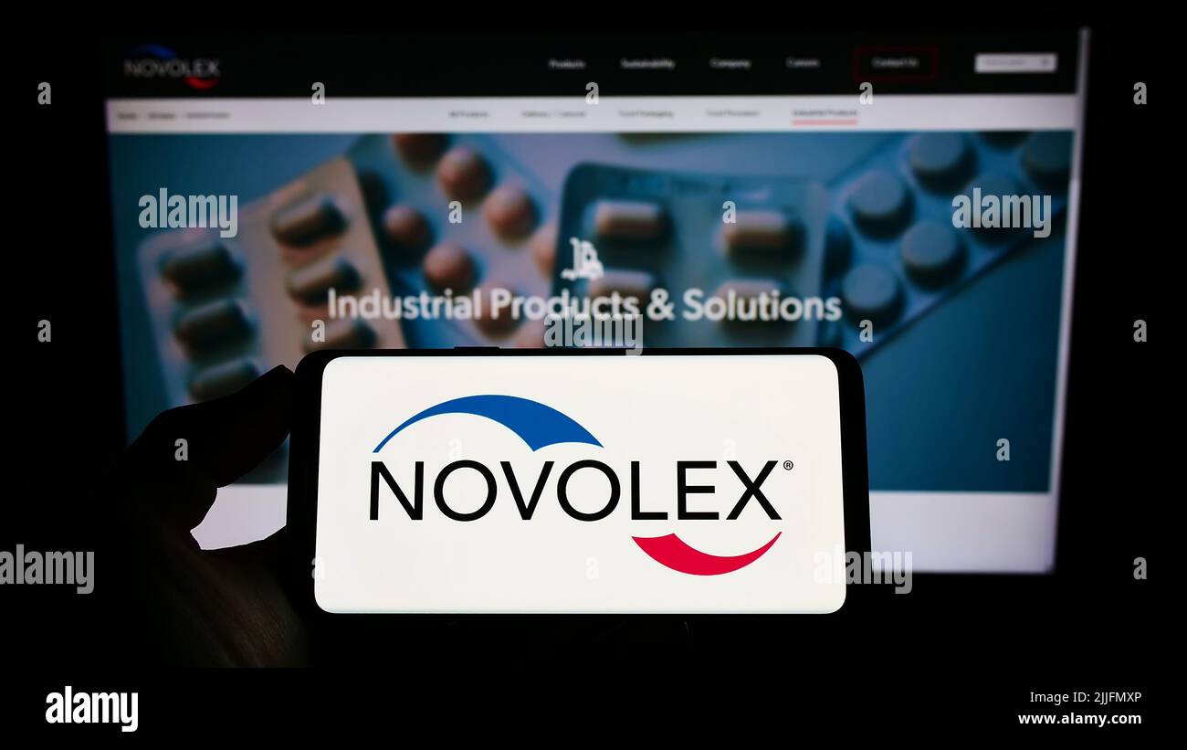 Person holding mobile phone with logo of American packaging company Novolex Holdings LLC on screen in front of web page. Focus on phone display. Stock Photo