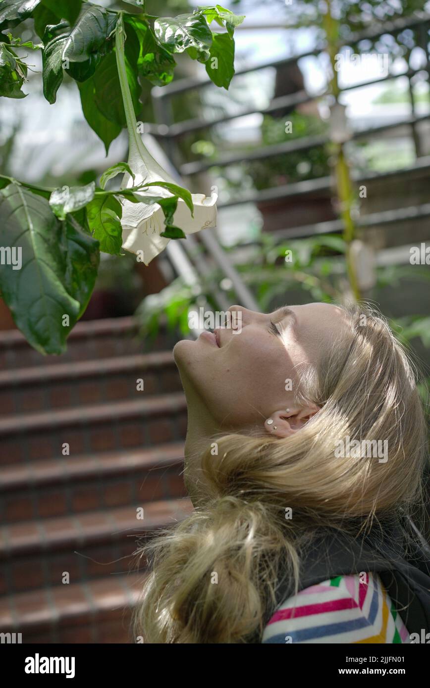 A vertical shot of a European girl with blonde hair smelling flowers outdoors Stock Photo