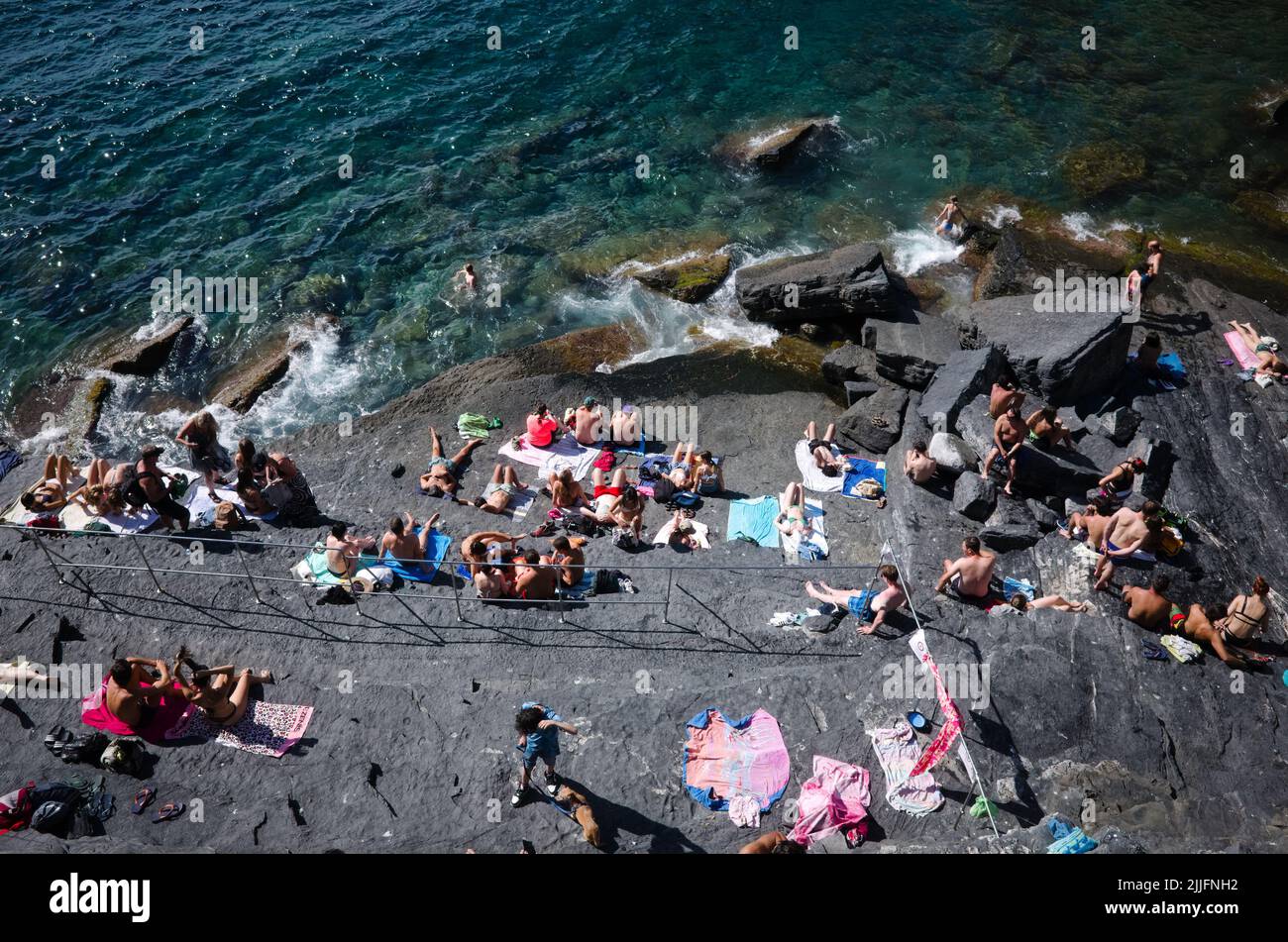 Porto Venere, Liguria, Italy - July, 2022: People sunbathe on rocks on Mediterranean coast of Italian Riviera. Wild beach on rocks on coast of Liguria Stock Photo