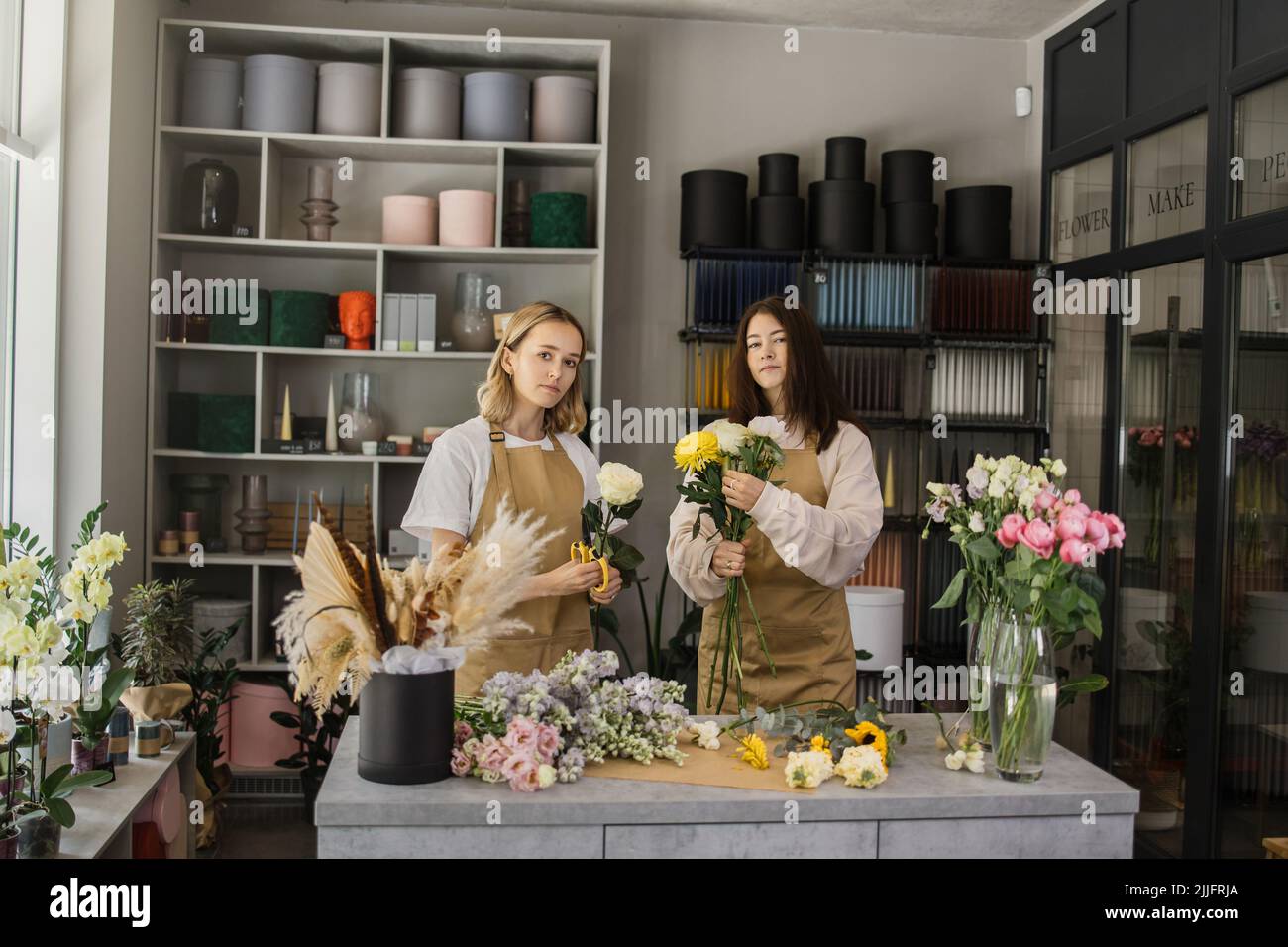 Two smiling florists in uniform work in a flower shop behind counter