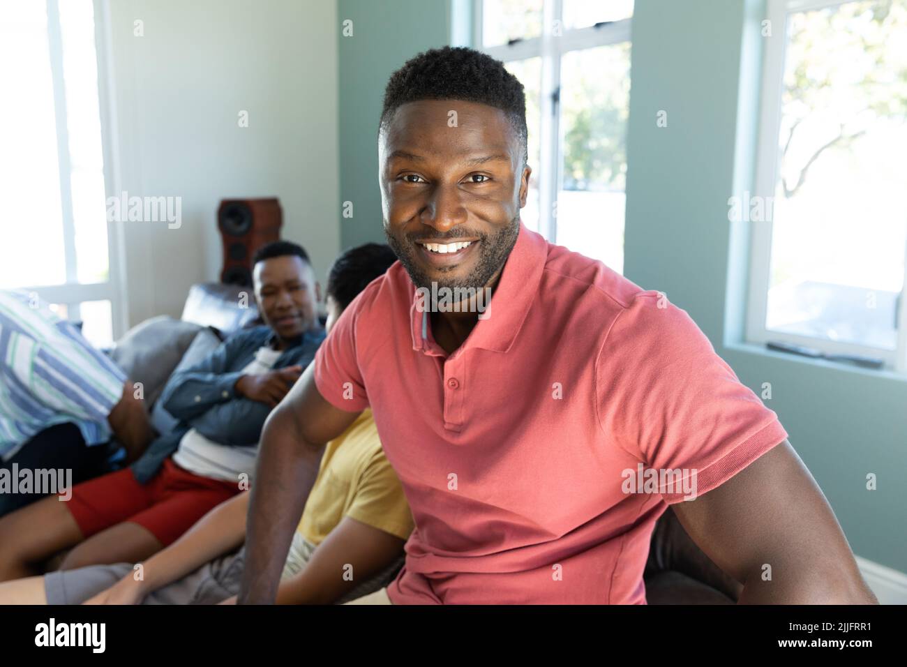 Portrait of smiling young man with multiracial male friends sitting on sofa in background at home Stock Photo