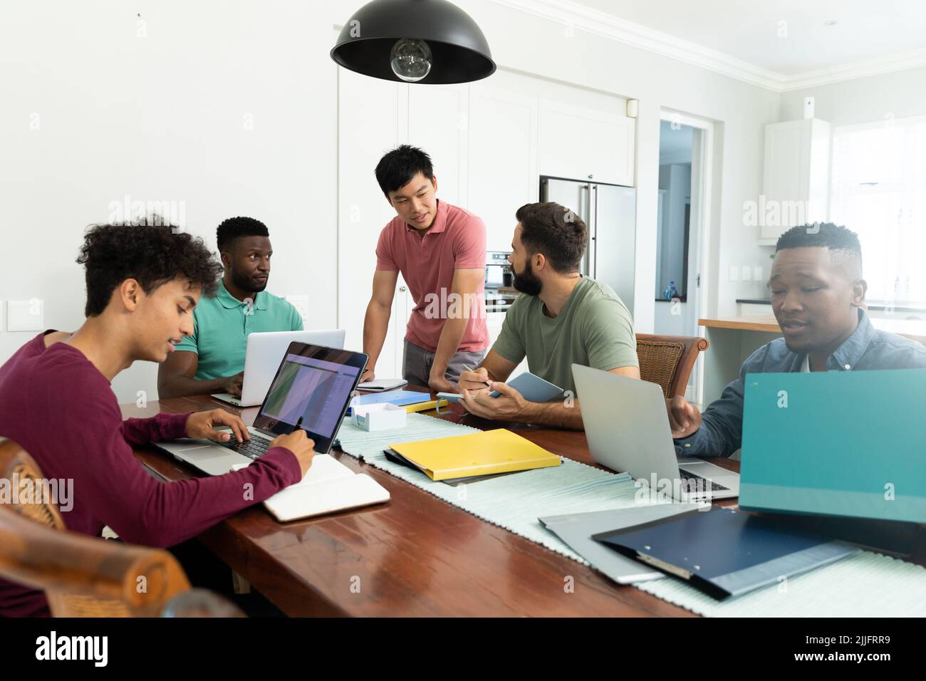 Multiracial male colleagues discussing and co-working over laptops on desk in office, copy space Stock Photo