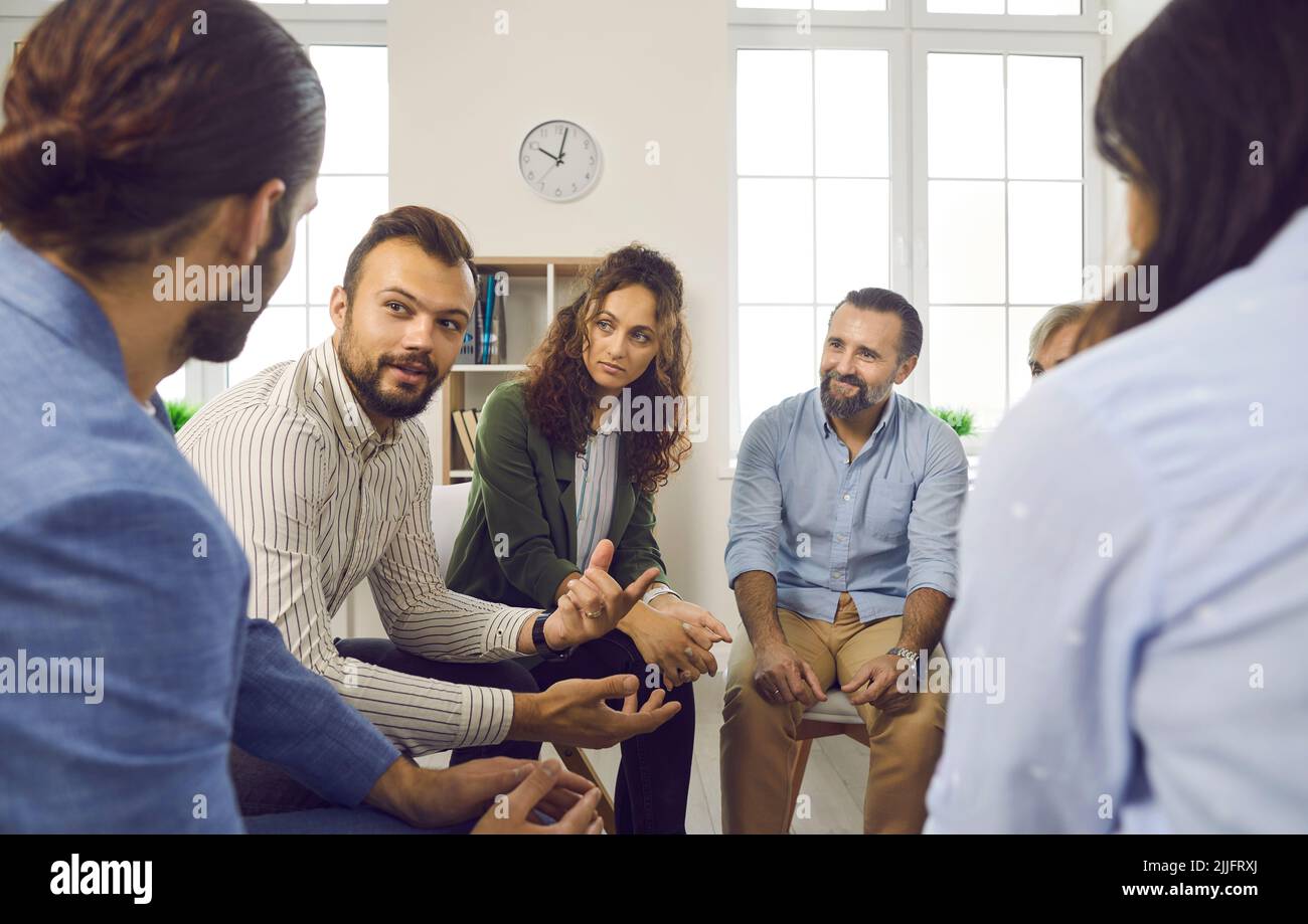 Different men and women at support group meeting listen to young man talking about himself. Stock Photo