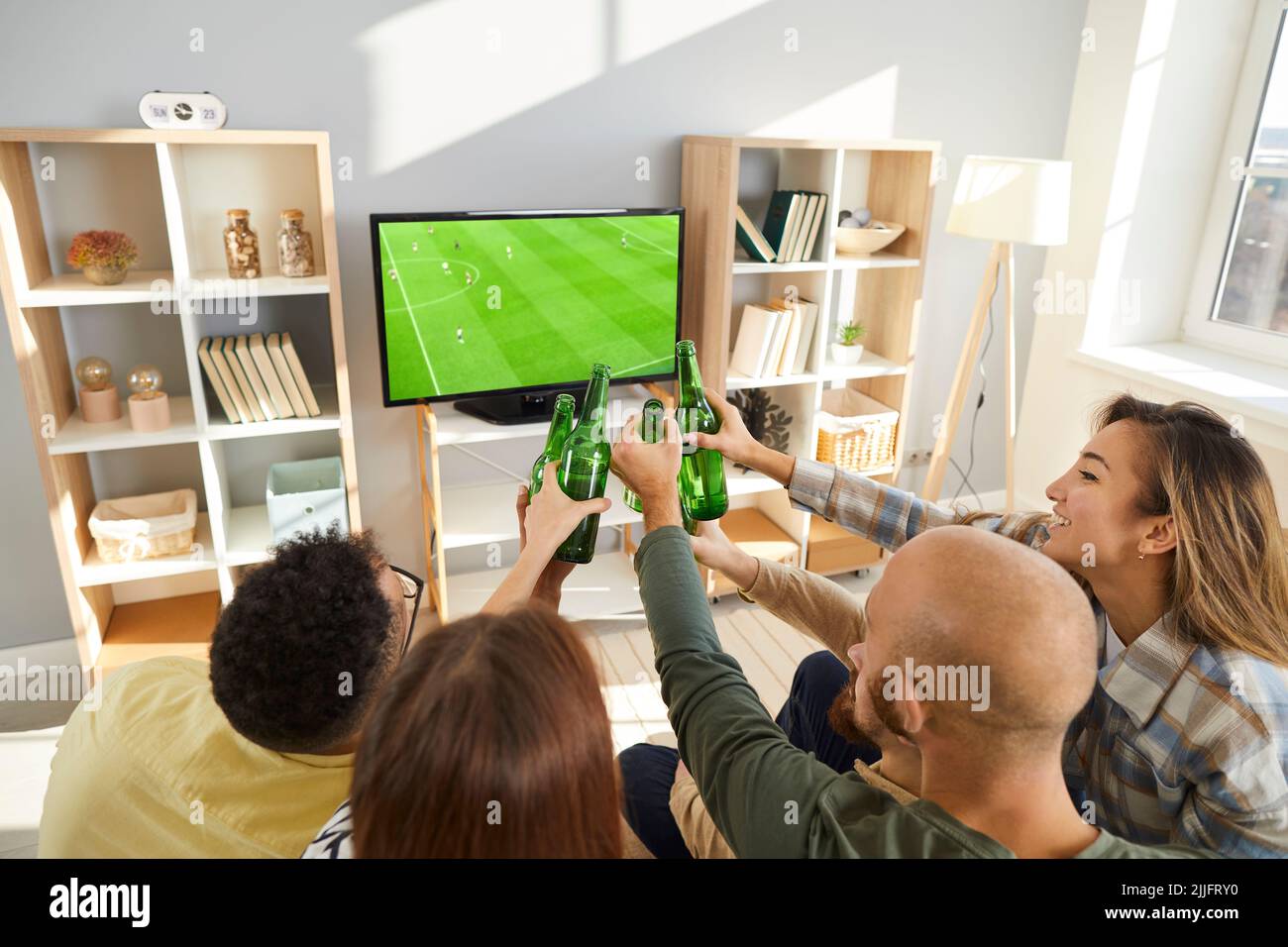 Happy young friends clinking beer bottles while watching football match together Stock Photo