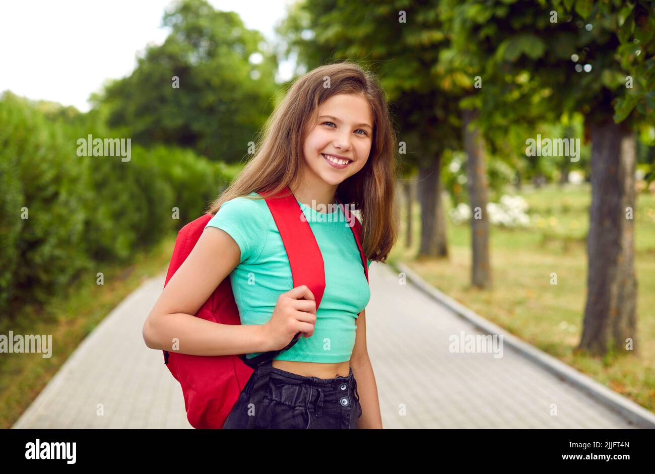 Portrait of happy, smiling teenage school girl with backpack standing in the park Stock Photo