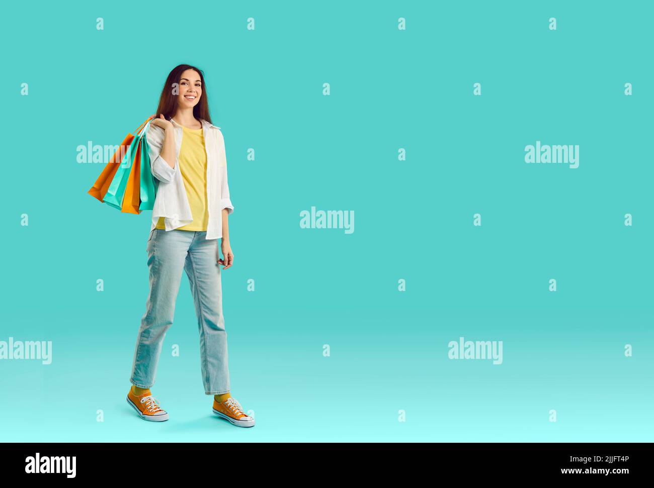 Happy young woman with shopping bags standing on turquoise copy space studio background Stock Photo