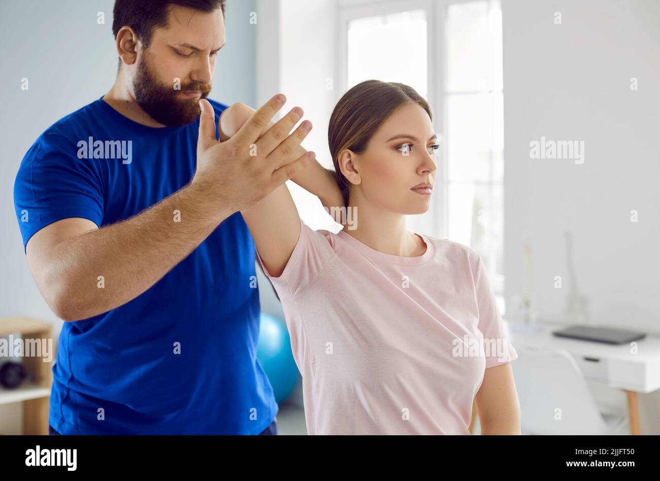 Serious male physiotherapist examines injured arm of female patient in medical clinic. Stock Photo