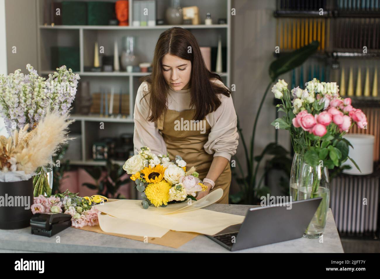 Gardeners in the flower shop make bouquet for a holiday and wraps it in kraft paper. Family
