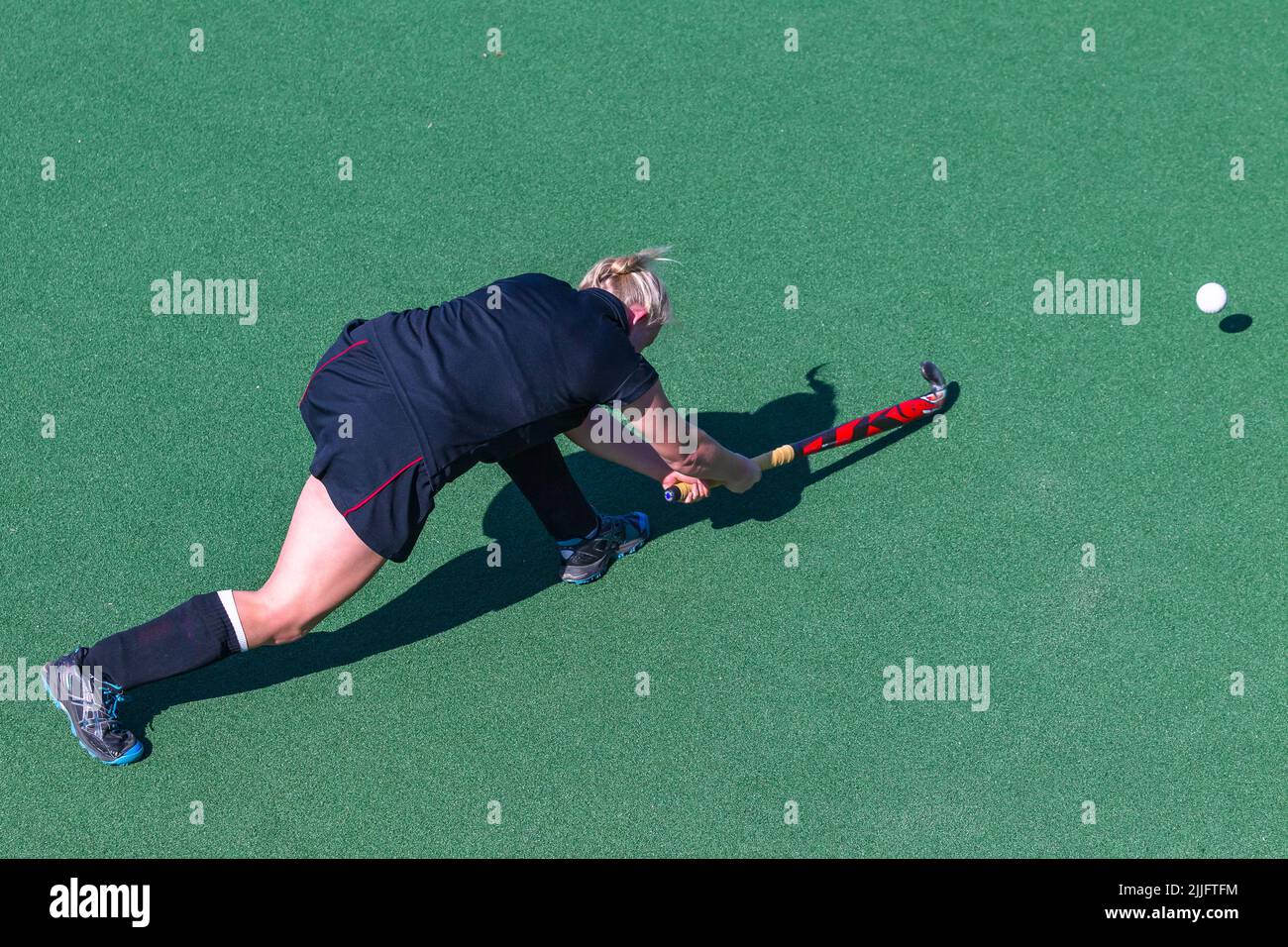 Hockey game girl player pushes pass the ball on astro turf overhead action photo. Stock Photo