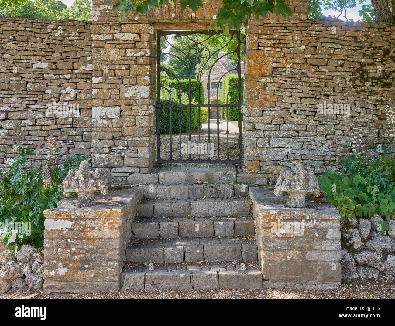 Stone steps leading to a wrought Iron garden gate in a traditional cotswold stone garden wall Stock Photo