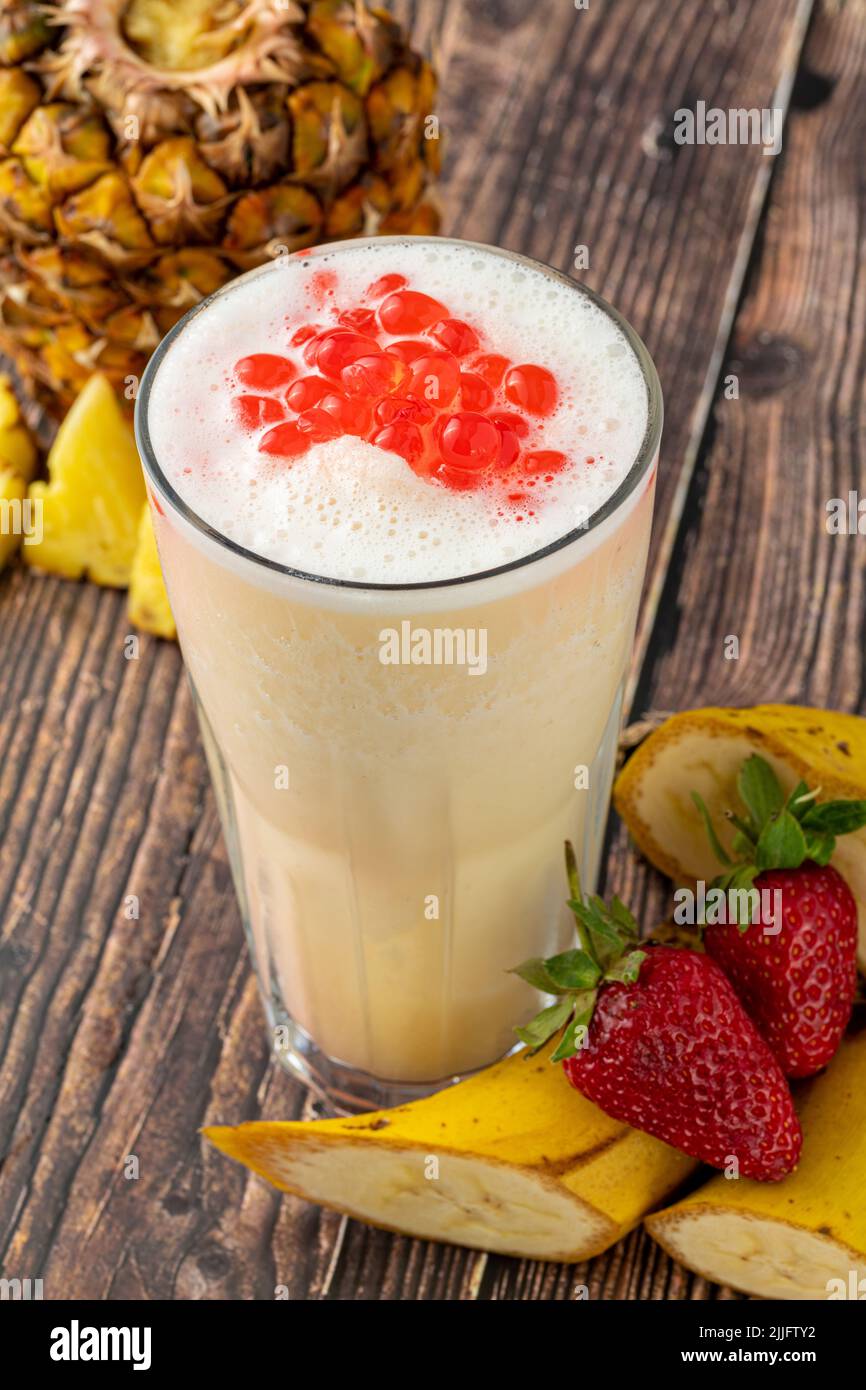 Banana, strawberry and pineapple smoothie on wooden table and bubble tea or boba tea balls on it Stock Photo