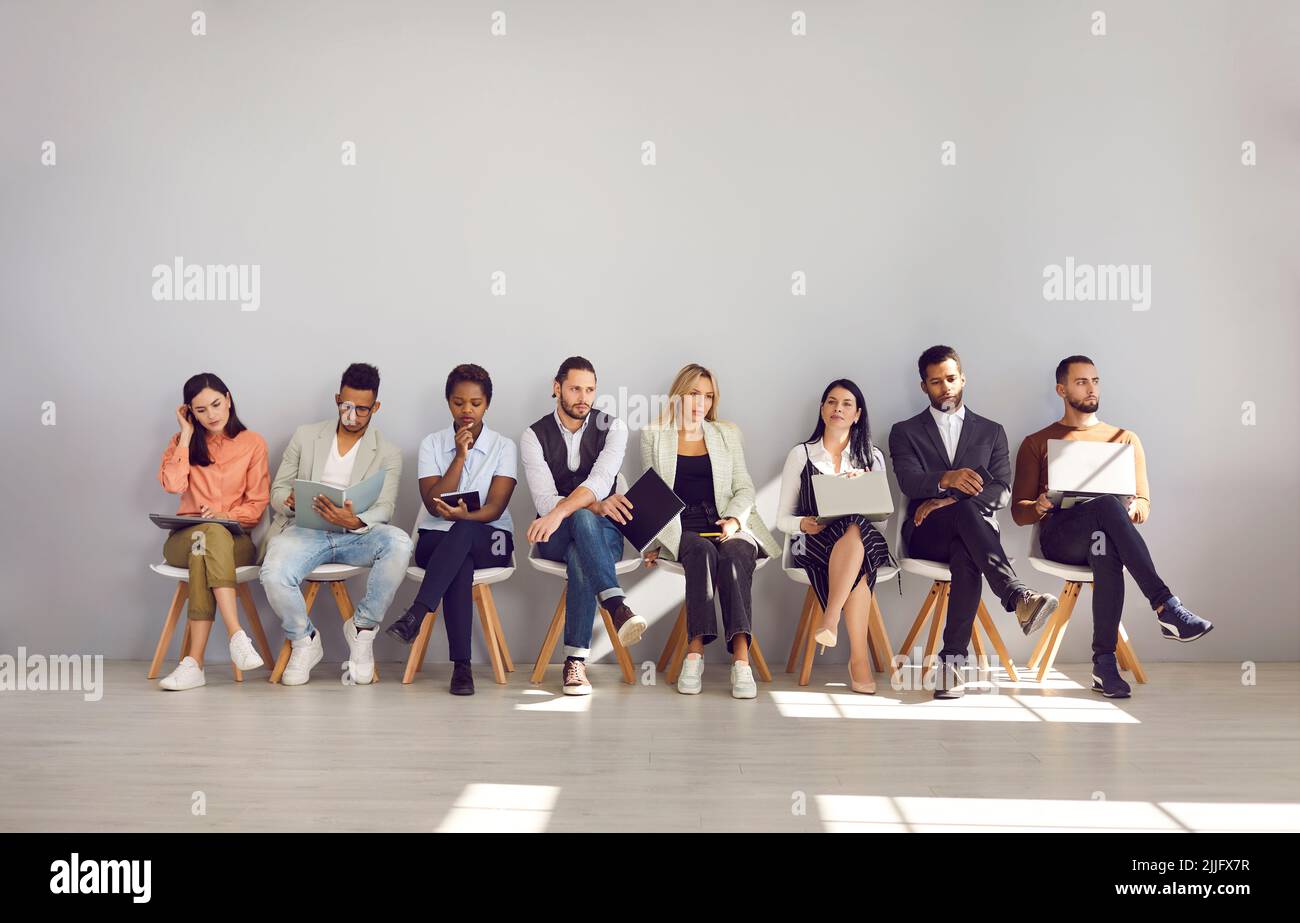 Group of multiracial people are waiting their turn for interview sitting on chairs in row. Stock Photo