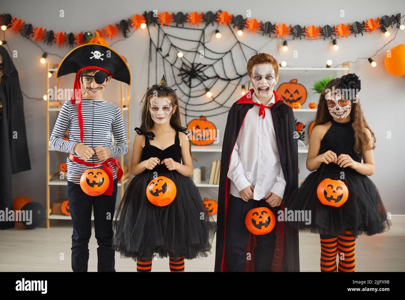 Group of children in different spooky Halloween costumes holding pumpkin baskets Stock Photo