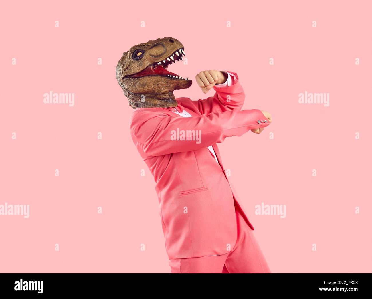 Cheerful funny and humorous man in dinosaur rubber mask dances isolated on pastel pink background. Stock Photo