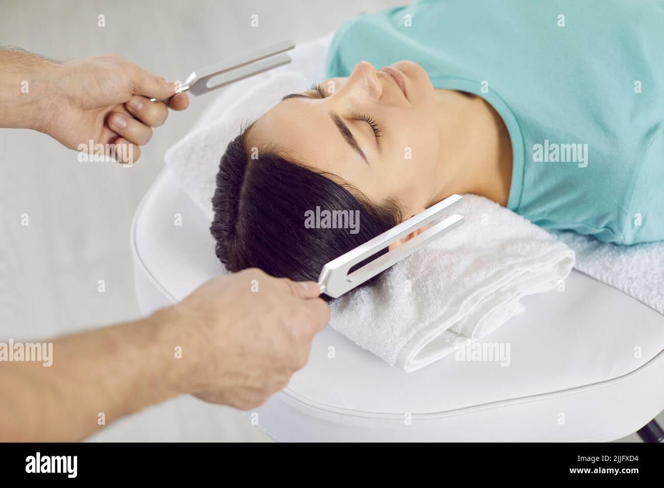 Specialist healing young woman with help of tuning forks and holistic
